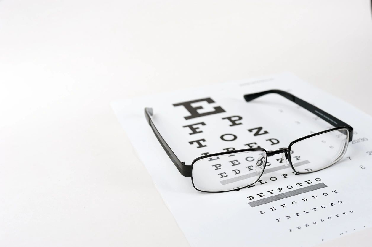 A pair of black metal glasses lay on a piece of paper. The paper is a Snellen Chart used for doctors to test a patient's vision.