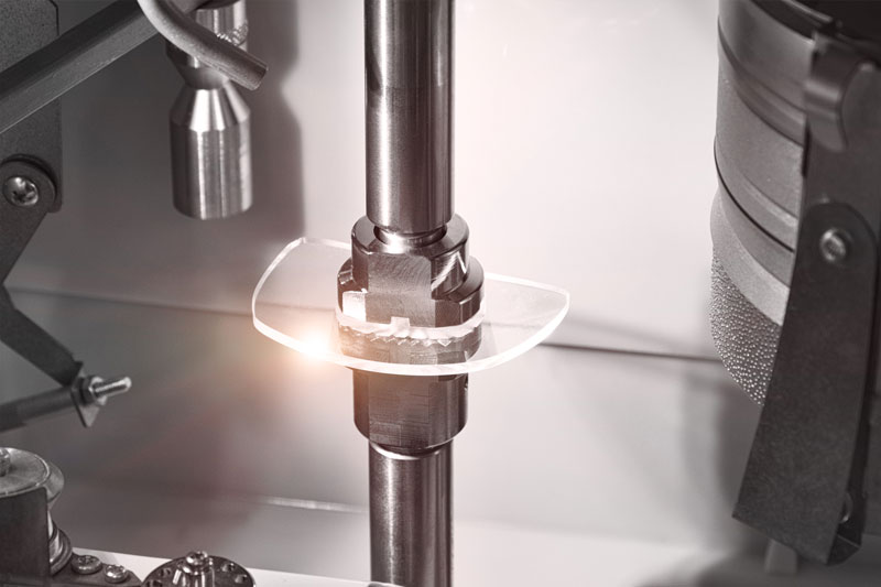 A cut lens from a pair of glasses sits compressed between two metal farms. It appears that this lens was recently cut to fit a pair of glasses.